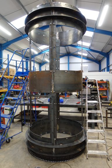 Industrial vertical structure with metal framework, surrounded by tools and equipment in a workshop.